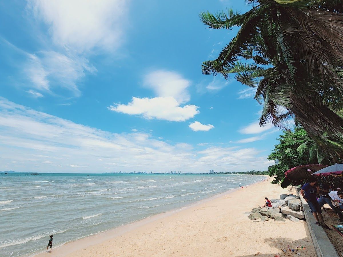Bang Saray Beach — wide sandy shore curving south with palm trees and the Pattaya skyline on the horizon