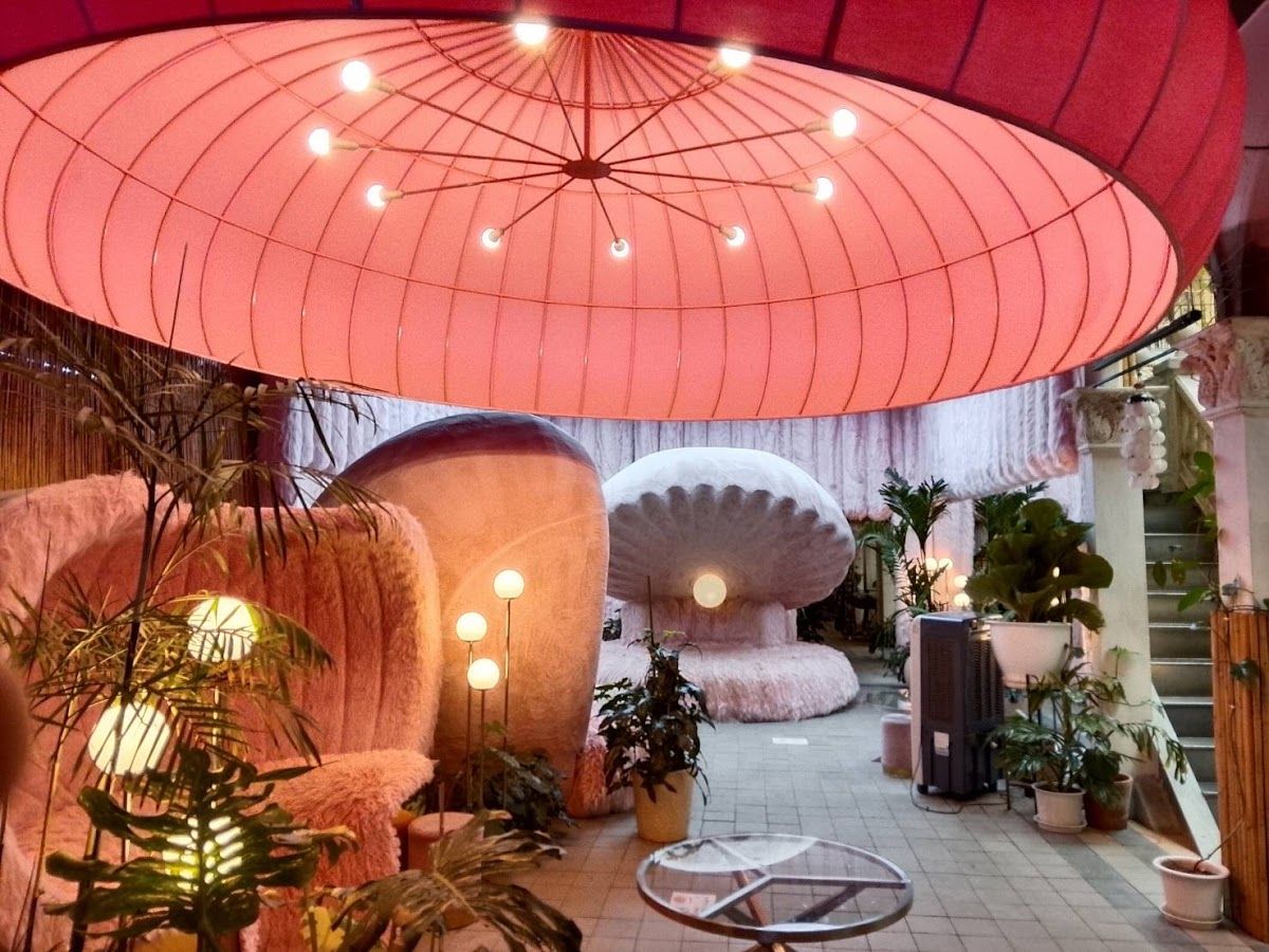 Rooftop cafe terrace with tables overlooking Pattaya Bay at golden hour with warm pink and orange sky