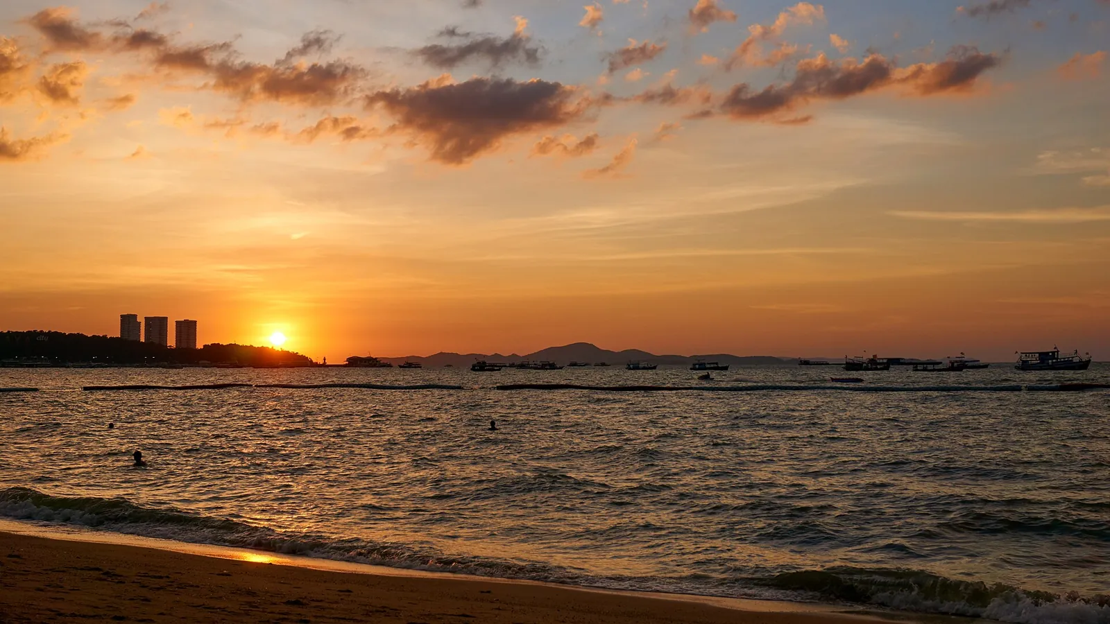 Fishing boats on Pattaya Beach at sunset with the sun on the horizon