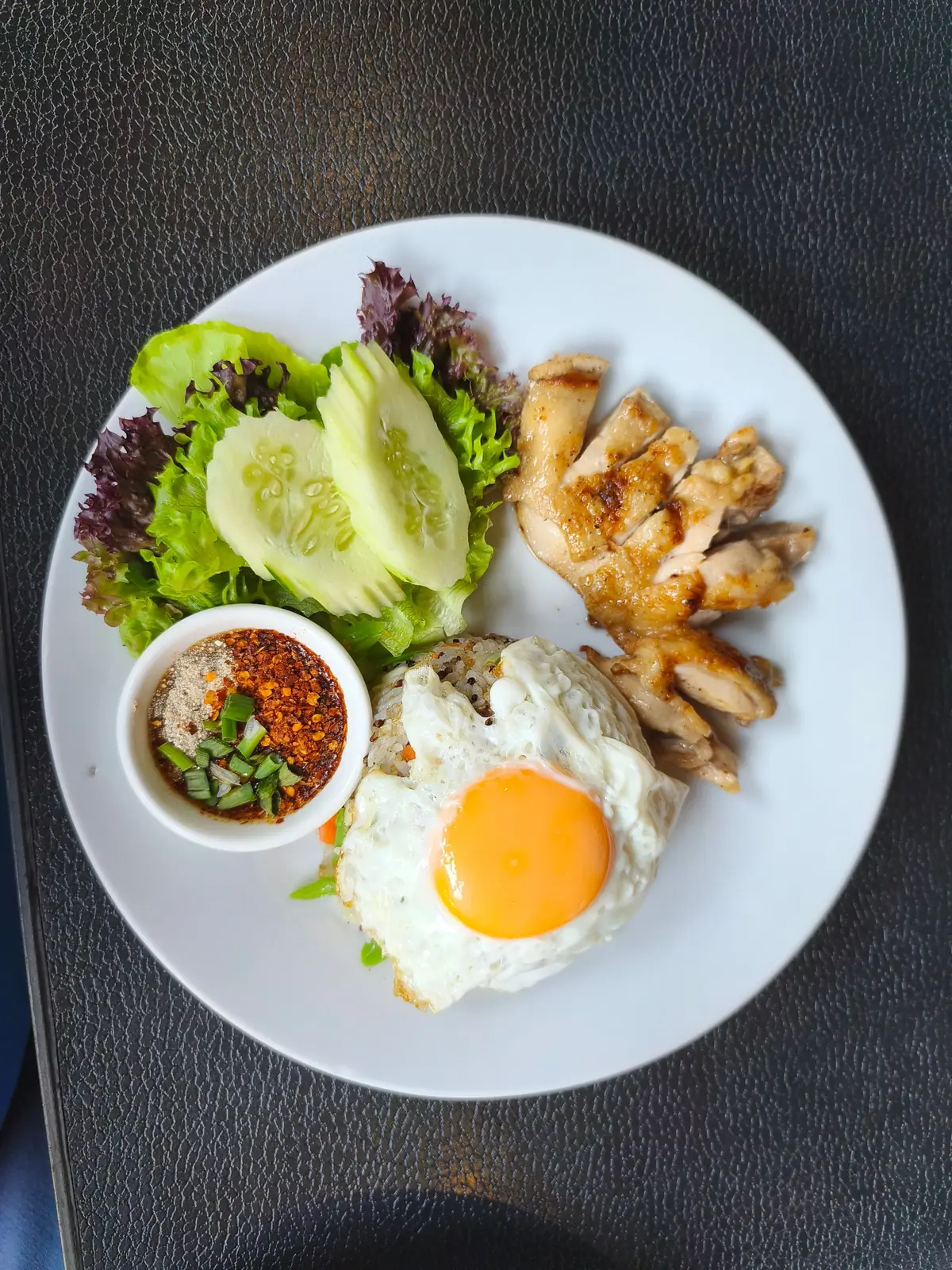 A plate of Thai chicken rice with a fried egg, cucumber and chilli sauce