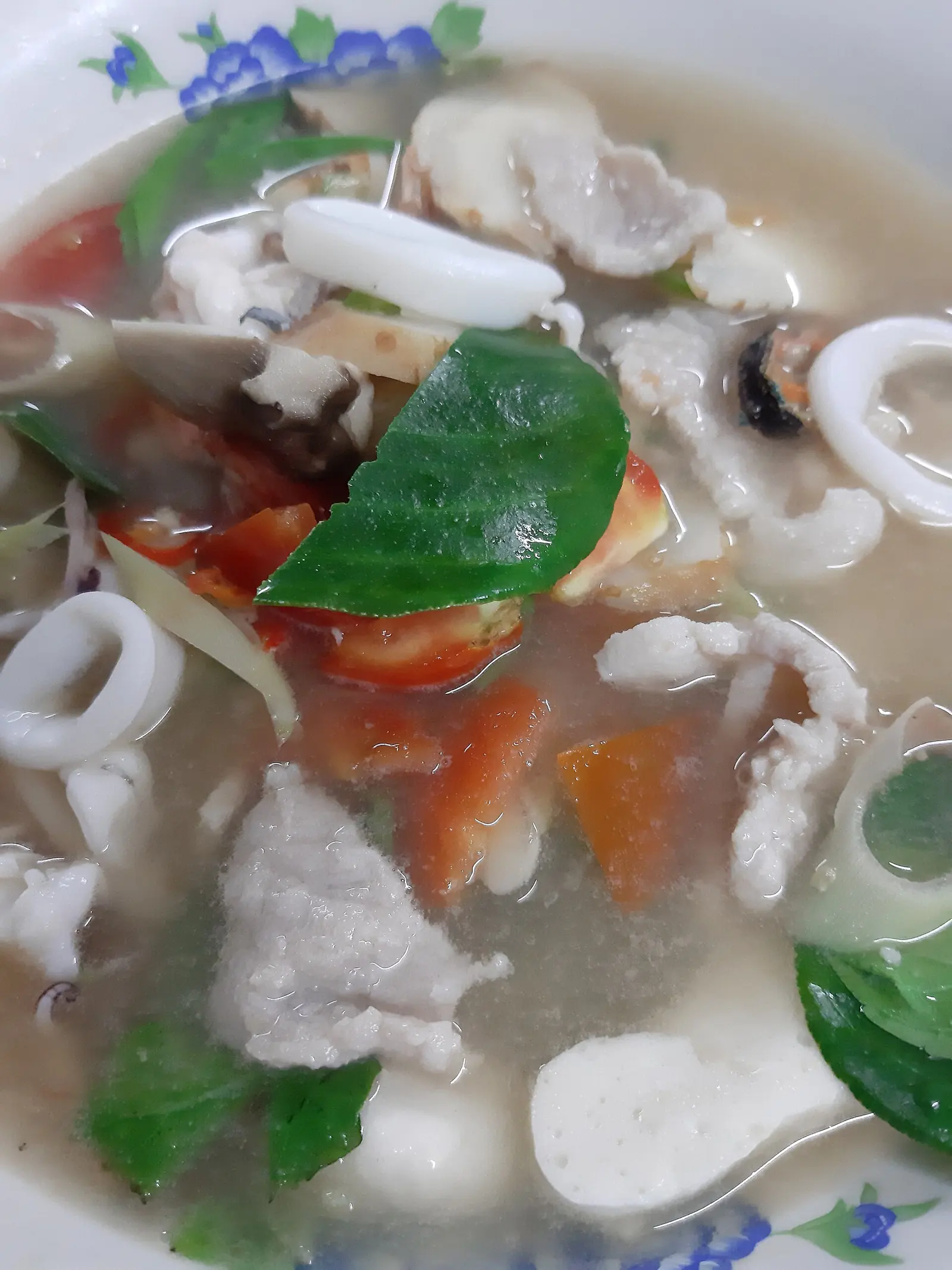 A bowl of tom yum soup with prawns, mushrooms and herbs