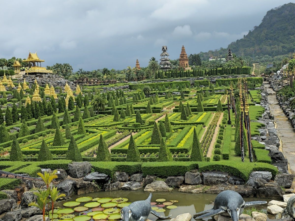 Nong Nooch Tropical Garden's French-inspired formal garden with manicured topiary hedges, a lily pond, golden temple pagodas and mountains in the background