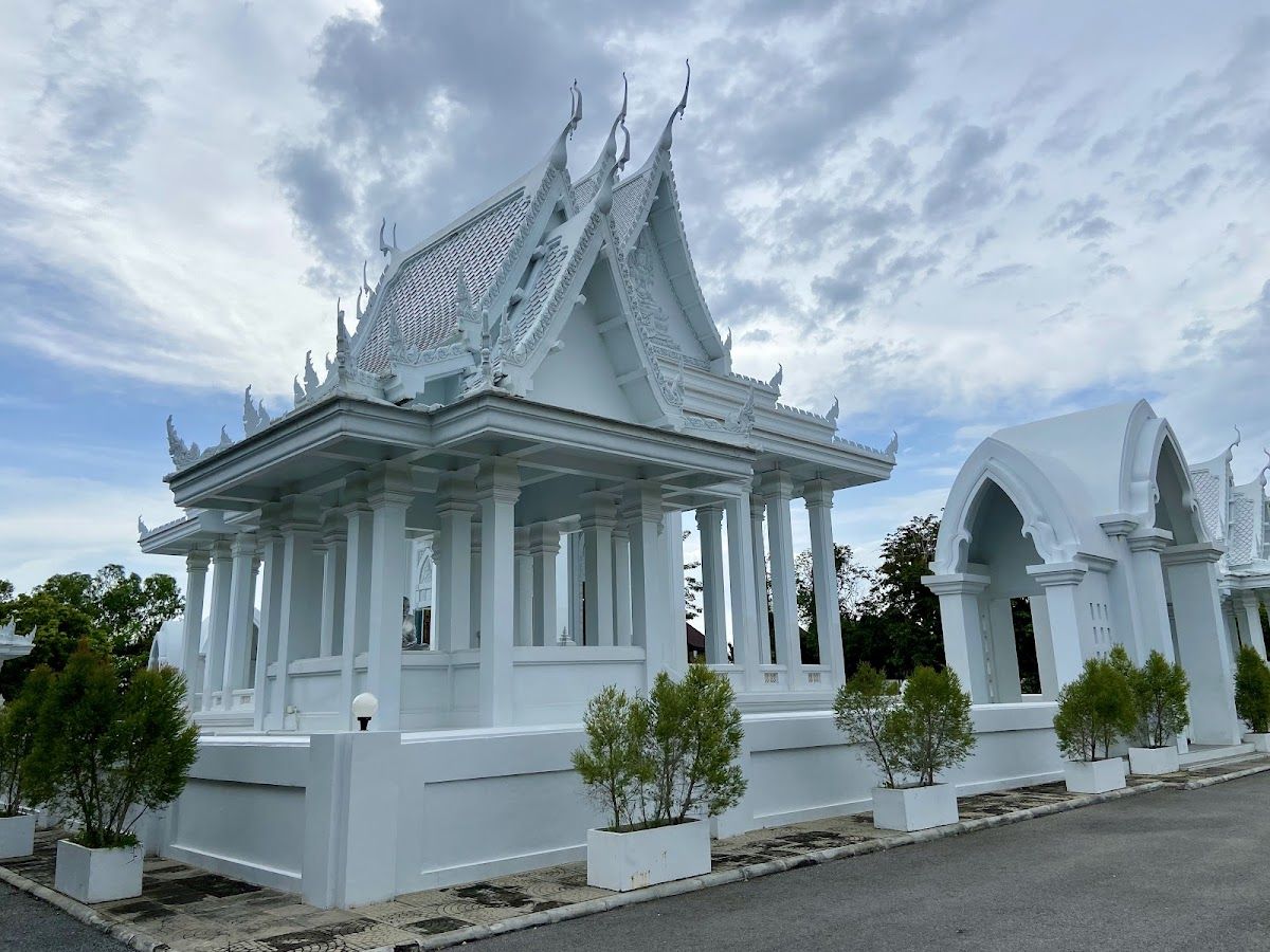Ornate white and gold temple gate at Wat Yansangwararam, Pattaya, under a bright blue sky with visitors walking through