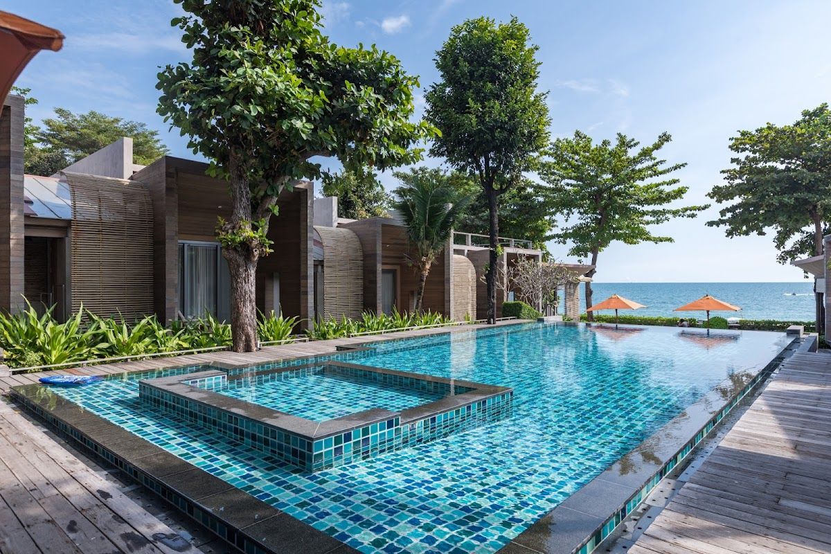 White sand Sai Kaew Beach on Koh Samet with beach umbrellas and wooden sunbeds lined up along the shoreline, turquoise water and palm trees behind